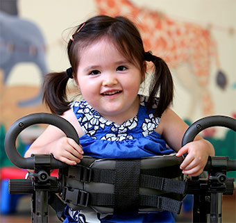 A young girl with cerebral palsy receives early intervention gait training services while walking in a pink Pacer.