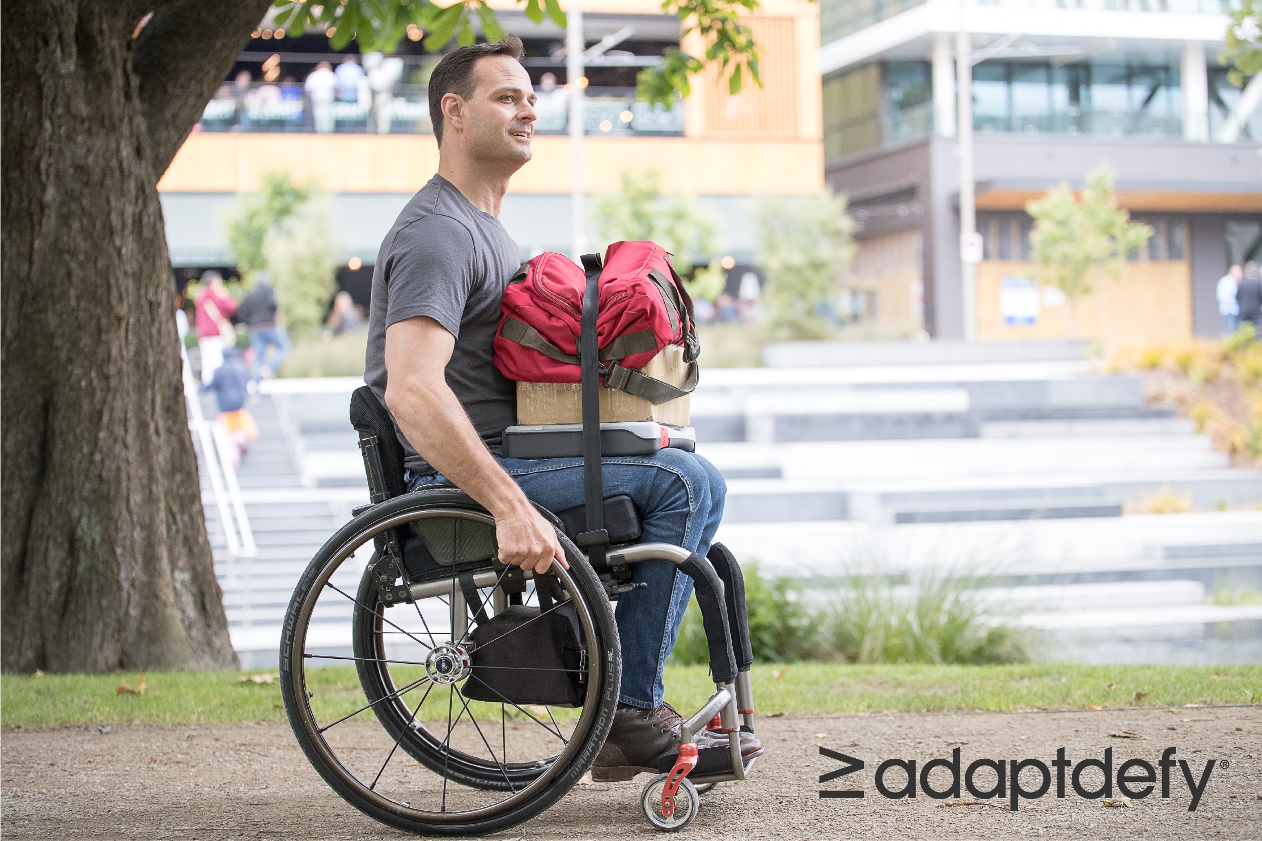 Man in manual wheelchair using carrying device to secure a bag and other items to his lap while pushing