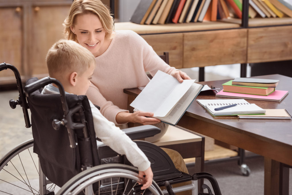 woman holds up a book for disabled child in the classroom
