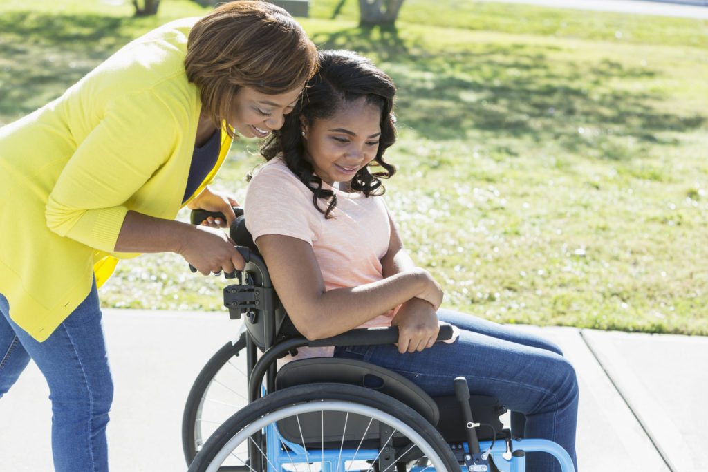 woman helps push a girl in a wheelchair down the sidewalk