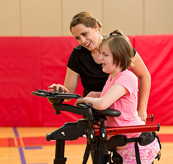 A young teenager standing in a Rifton Pacer Gait Trainer doing and activity with a caregiver.