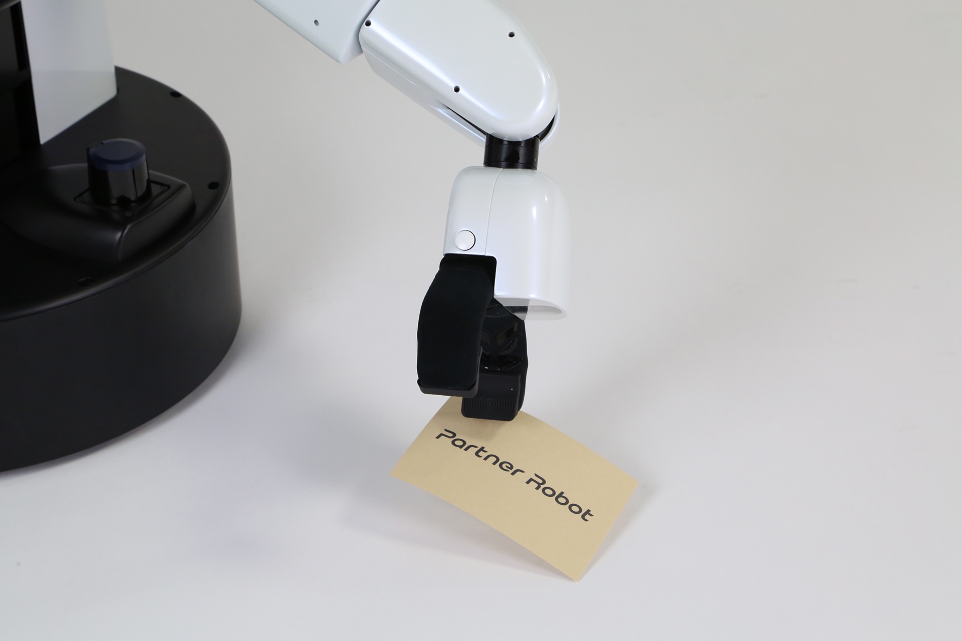 Toyota's "HSR" personal care robot uses a suction cup to pickup a business card with the text "Partner Robots" 