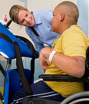 A young man works on toileting transfer skills using the Rifton Support Station while his therapists provides guidance.