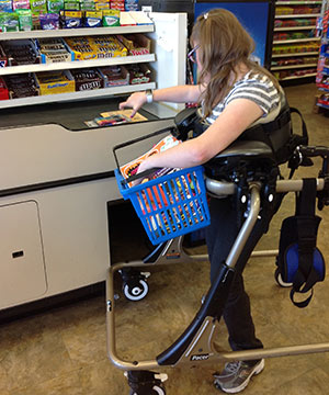 A young woman stands at the checkout counter in her adaptive equipment to check out her items as part of an assignment in the transitional program.