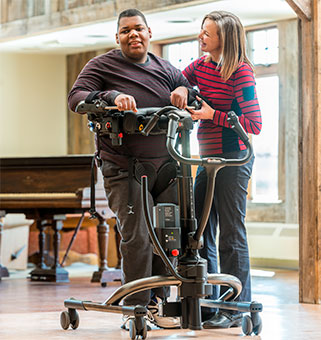 A therapist practices safe patient handling and mobility while using the Rifton TRAM to support a young man during gait training.