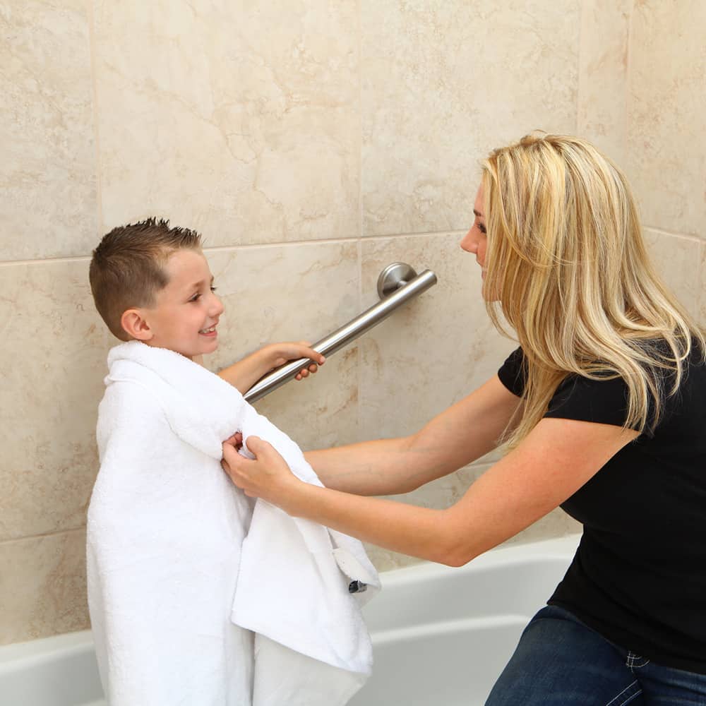 Woman drying off a boy as he uses a grab bar for stability in the bathtub