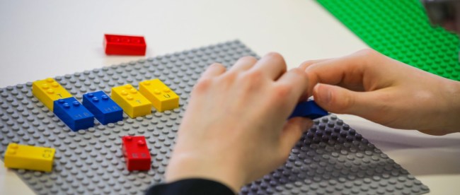 close up of a child's hands shown playing with braille lego blocks. Braille legos will have letters, numbers and punctuation printed on them as well so both sighted and blind children can play together.