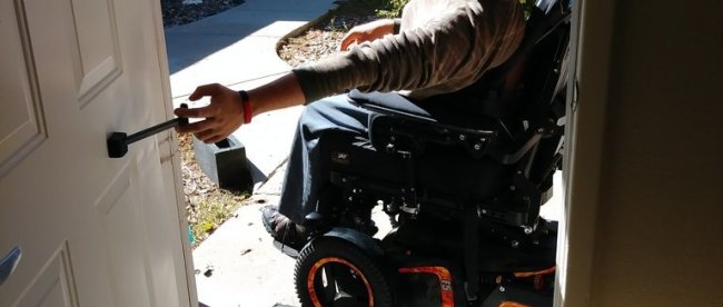 a man in a motorized wheelchair seen pulling on the t-pull door closer attached to a door.